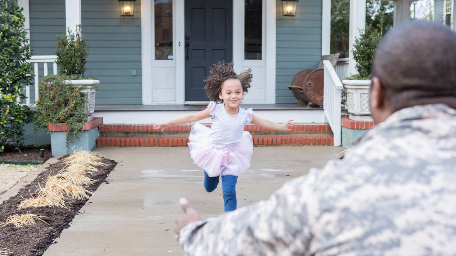 A young girl sprints towards her father, an African-American man donning the distinguished attire of a military uniform. Her arms are wide open, mirroring the grin that stretches across her face. Her outfit is a medley of childhood favorites: a white T-shirt, a frilly pink tutu, and trusty blue jeans. The soldier, her father, is a blur in the background, only the back of his head and a sliver of his shoulder visible, but his arms are outstretched, ready to embrace his little girl.